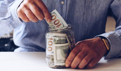 man putting $100 bills into a mason jar