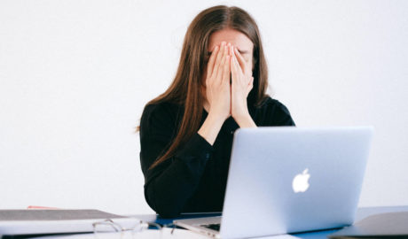 Stressed woman with hands over face in front of laptop