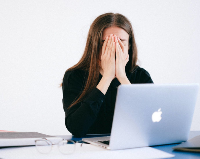 Stressed woman with hands over face in front of laptop