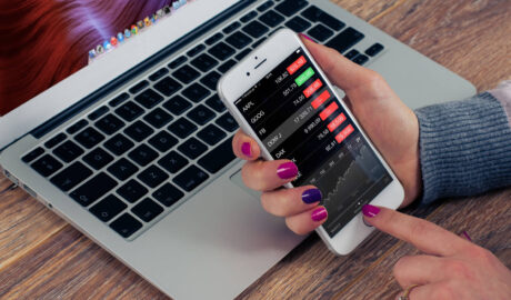 Person checking stock prices on phone in front of laptop