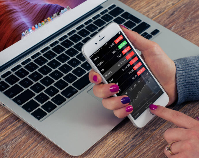 Person checking stock prices on phone in front of laptop