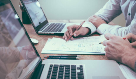 two people at laptops, see only their hands and a shared plan