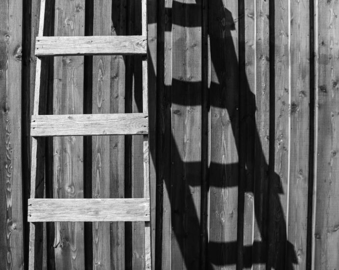 BW image of wooden ladder leaning up against side of building