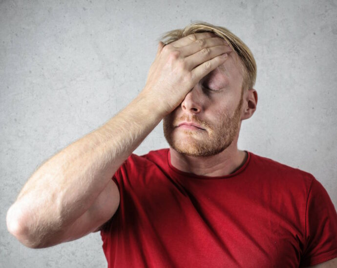 man in red shirt looking stressed with hand on forehead