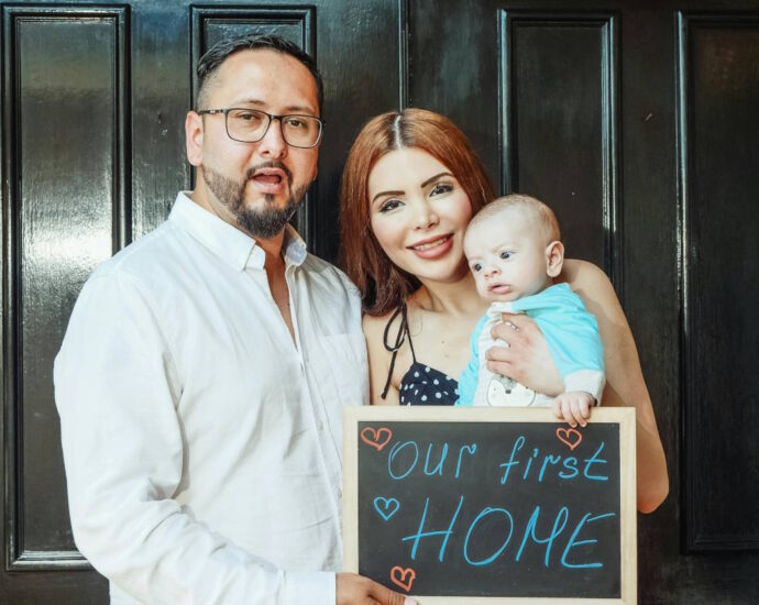 Couple with baby holding sign: "Our first home"