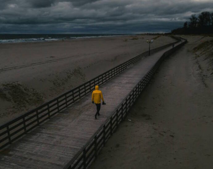 person in yellow raincoat walking along pier by the ocean under dark clouds