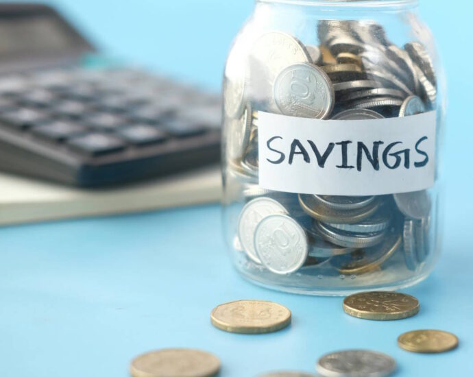 glass jar with coins labeled savings with calculator in background